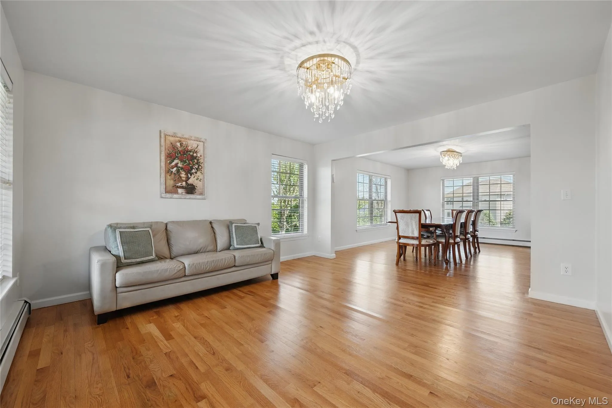 Living room with a chandelier, plenty of natural light, light wood finished floors, and baseboards Living room with a chandelier, plenty of natural light, light wood finished floors, and baseboards