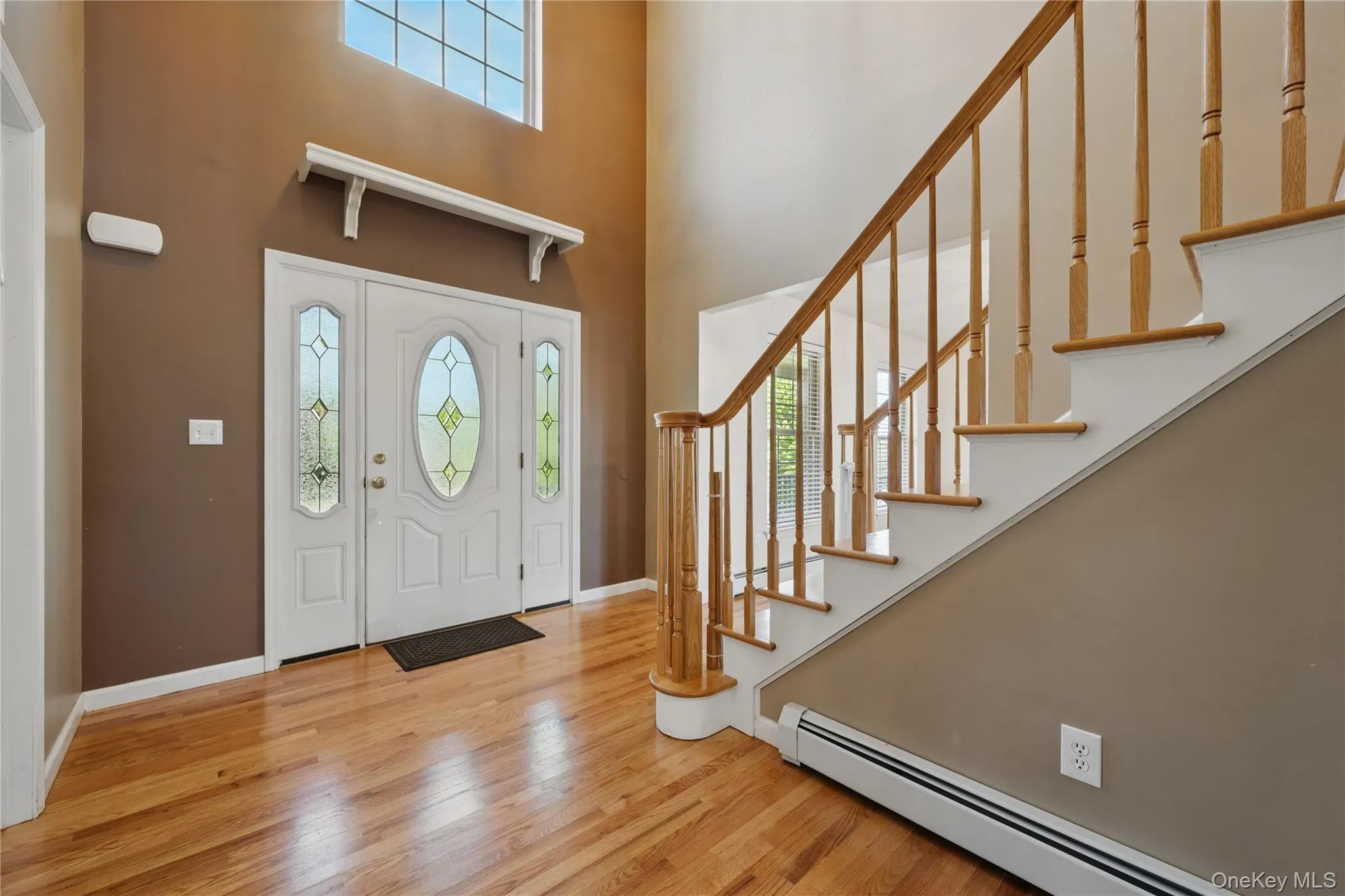 Entryway featuring a baseboard heating unit, a high ceiling, wood finished floors, baseboards, and stairway Entryway featuring a baseboard heating unit, a high ceiling, wood finished floors, baseboards, and stairway