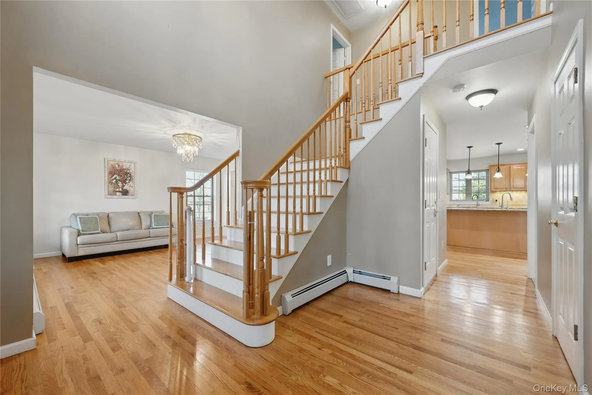 Stairs featuring wood finished floors, a towering ceiling, a chandelier, baseboard heating, and baseboards Stairs featuring wood finished floors, a towering ceiling, a chandelier, baseboard heating, and baseboards