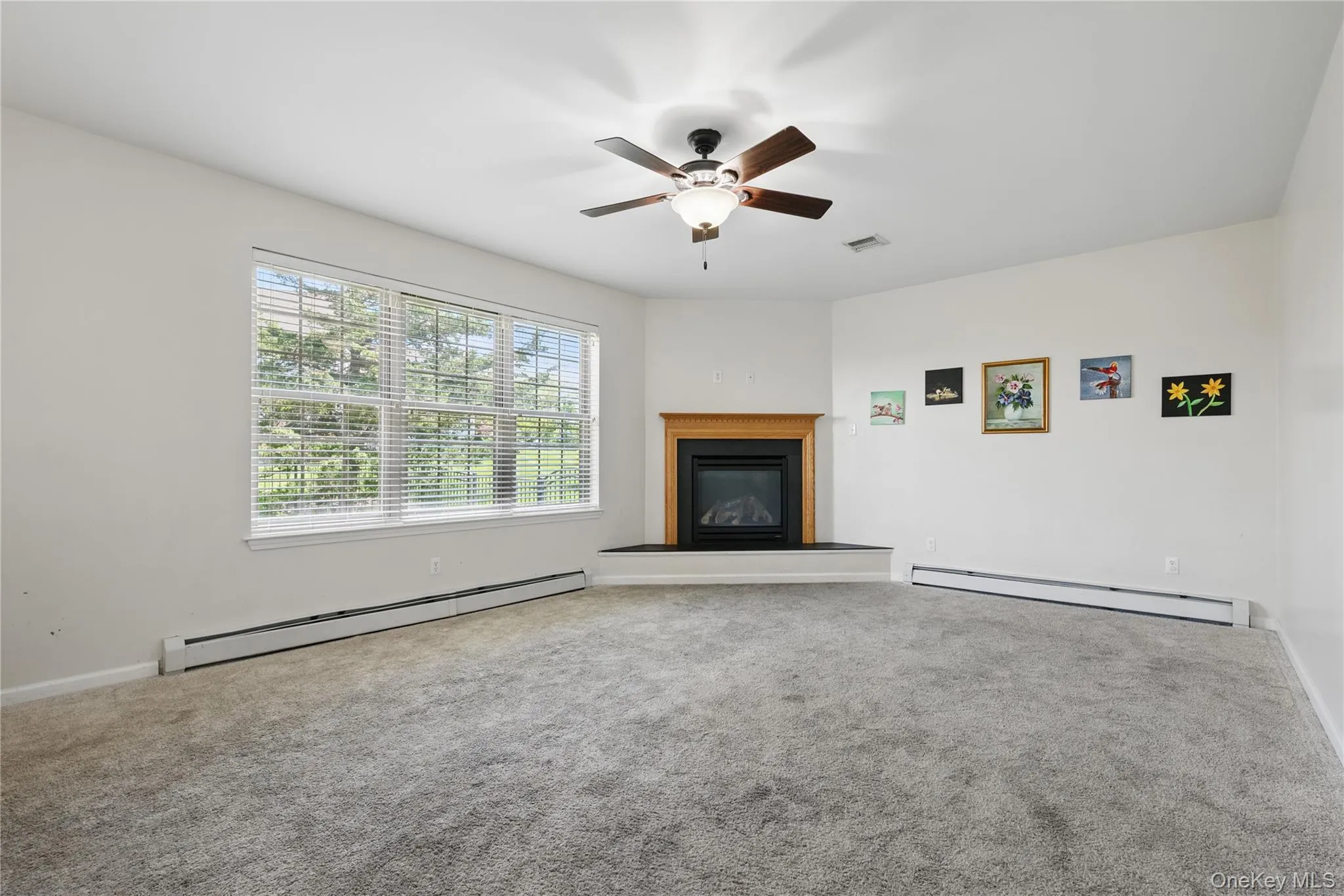 Unfurnished living room featuring a baseboard radiator, a glass covered fireplace, a ceiling fan, and carpet flooring Unfurnished living room featuring a baseboard radiator, a glass covered fireplace, a ceiling fan, and carpet flooring
