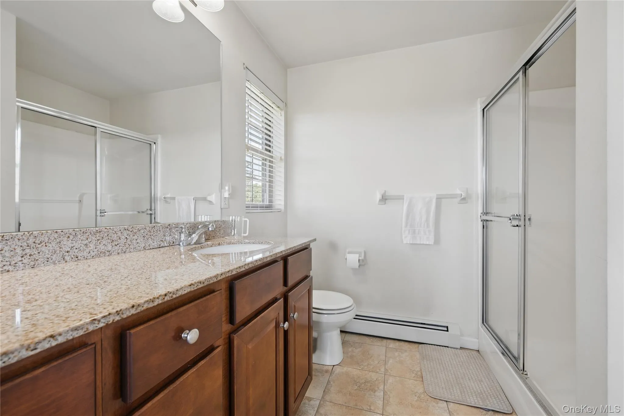 Bathroom featuring a baseboard heating unit, toilet, a stall shower, and vanity Bathroom featuring a baseboard heating unit, toilet, a stall shower, and vanity