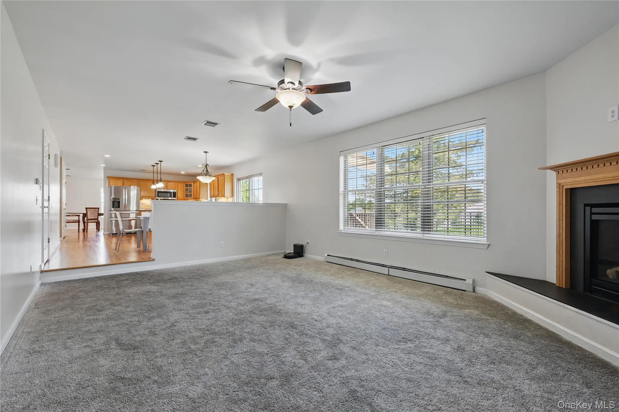 Unfurnished living room featuring baseboard heating, a ceiling fan, carpet flooring, a fireplace with raised hearth, and baseboards Unfurnished living room featuring baseboard heating, a ceiling fan, carpet flooring, a fireplace with raised hearth, and baseboards