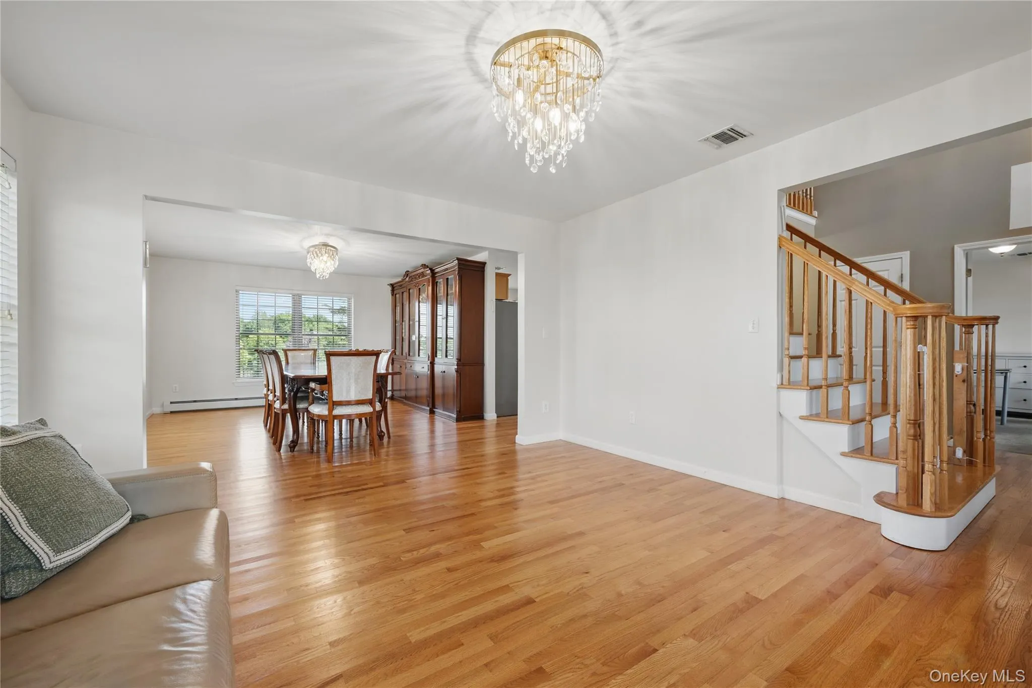 Living room featuring a chandelier, light wood-type flooring, baseboard heating, stairs, and baseboards Living room featuring a chandelier, light wood-type flooring, baseboard heating, stairs, and baseboards