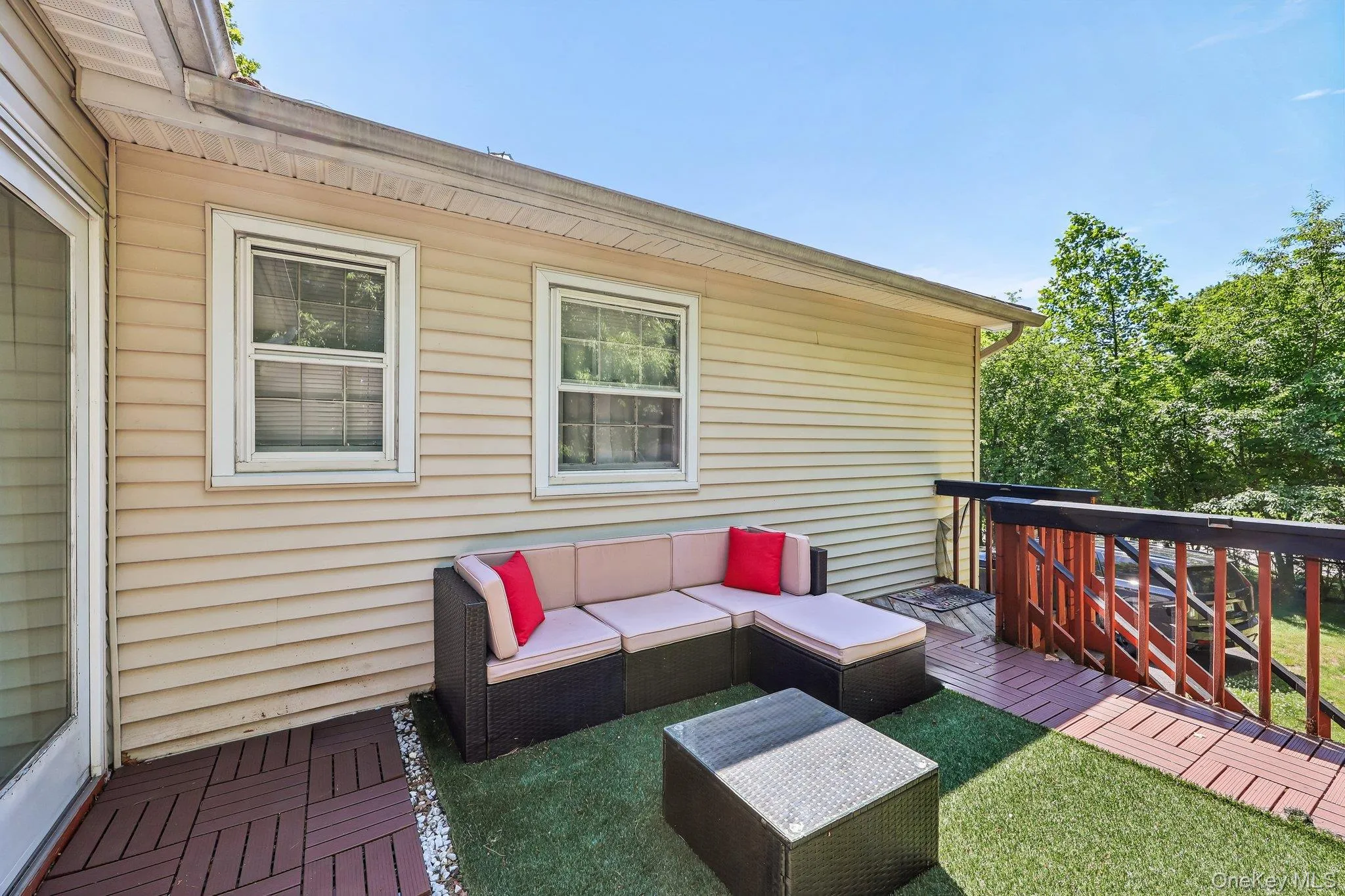 Expansive outdoor deck featuring wood-finish tile flooring, a slatted wood railing, and a section of artificial turf Expansive outdoor deck featuring wood-finish tile flooring, a slatted wood railing, and a section of artificial turf