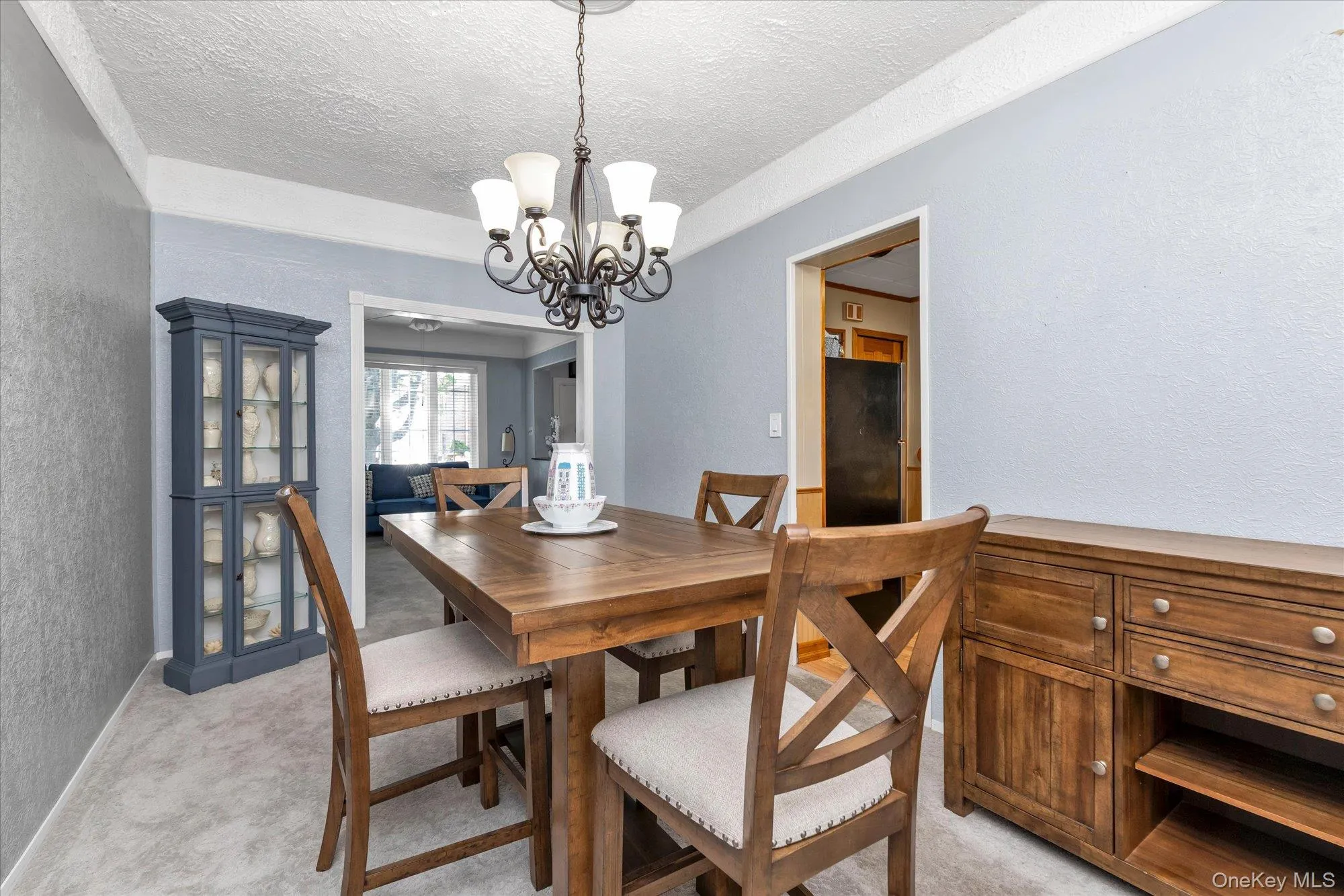 Dining area featuring a classic chandelier with frosted glass shades, a textured ceiling, and light blue wall tones Dining area featuring a classic chandelier with frosted glass shades, a textured ceiling, and light blue wall tones