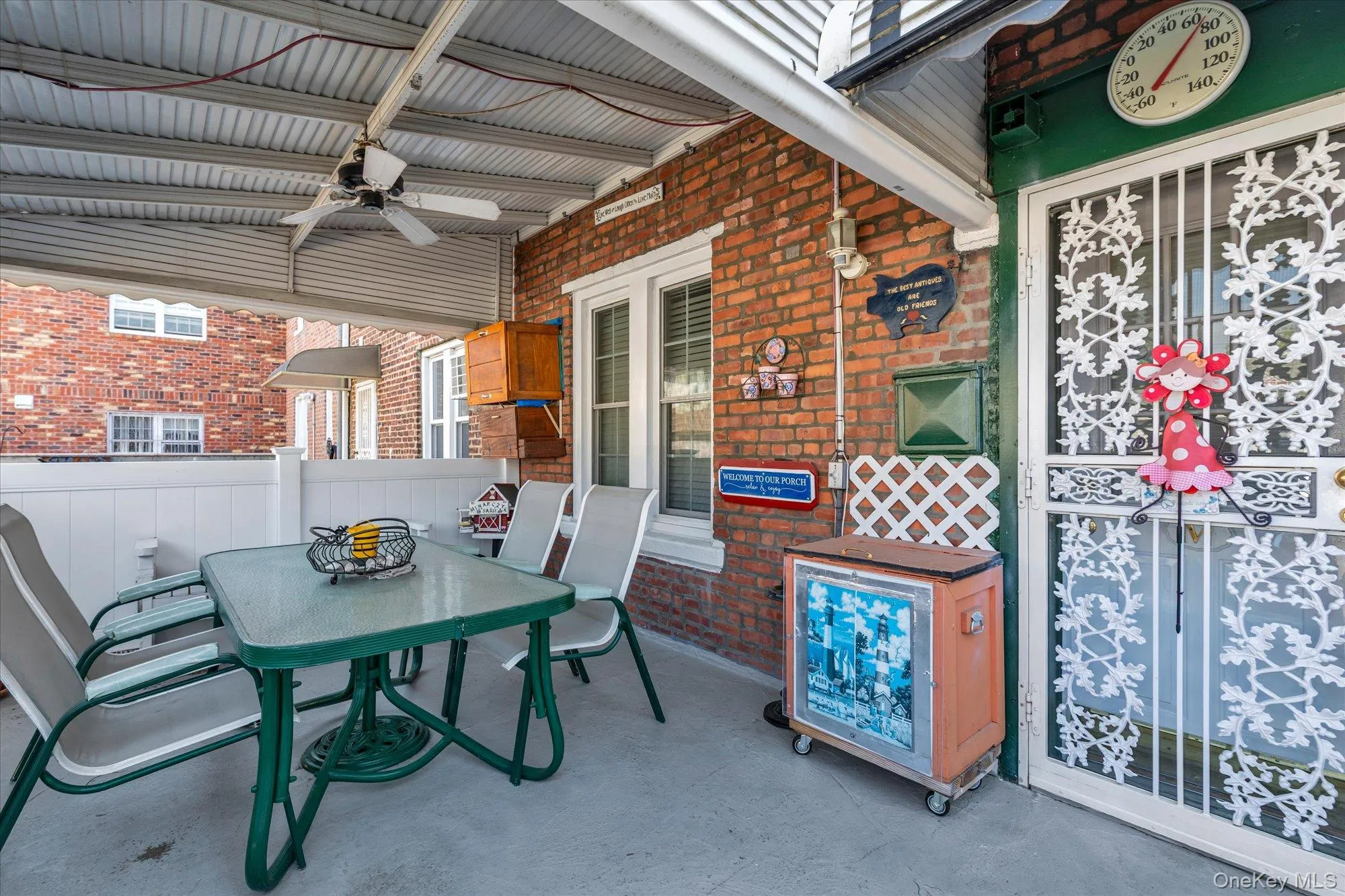 Covered patio featuring a corrugated metal ceiling with a ceiling fan, brick exterior wall, white picket railing, and a white security door with an ornate ironwork pattern Covered patio featuring a corrugated metal ceiling with a ceiling fan, brick exterior wall, white picket railing, and a white security door with an ornate ironwork pattern