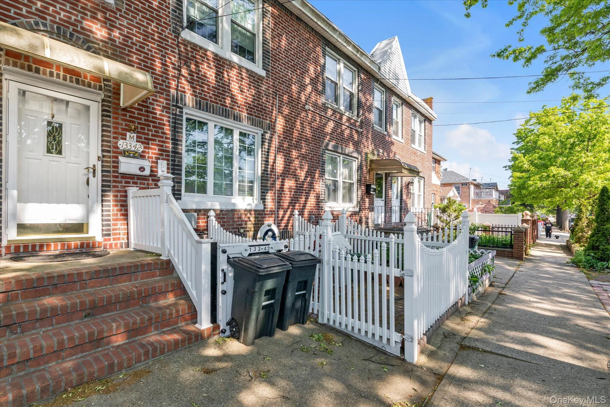 Brick facade residence featuring a front entrance with a white storm door, brick steps, and a white picket fence enclosing the front yard Brick facade residence featuring a front entrance with a white storm door, brick steps, and a white picket fence enclosing the front yard