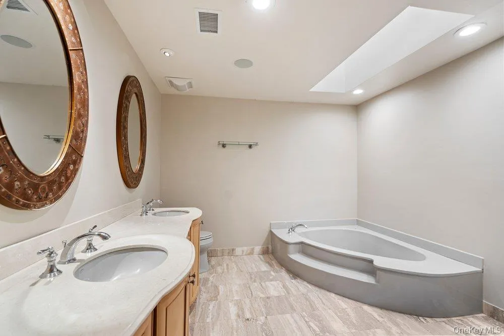 Bathroom featuring a built-in corner soaking tub, a skylight, and recessed lighting Bathroom featuring a built-in corner soaking tub, a skylight, and recessed lighting