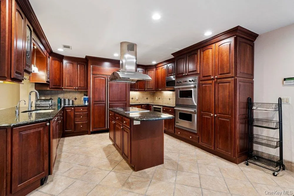 Gourmet kitchen featuring extensive dark wood cabinetry, granite countertops, tile flooring, stainless steel appliances, and a central island with a matching granite surface Gourmet kitchen featuring extensive dark wood cabinetry, granite countertops, tile flooring, stainless steel appliances, and a central island with a matching granite surface