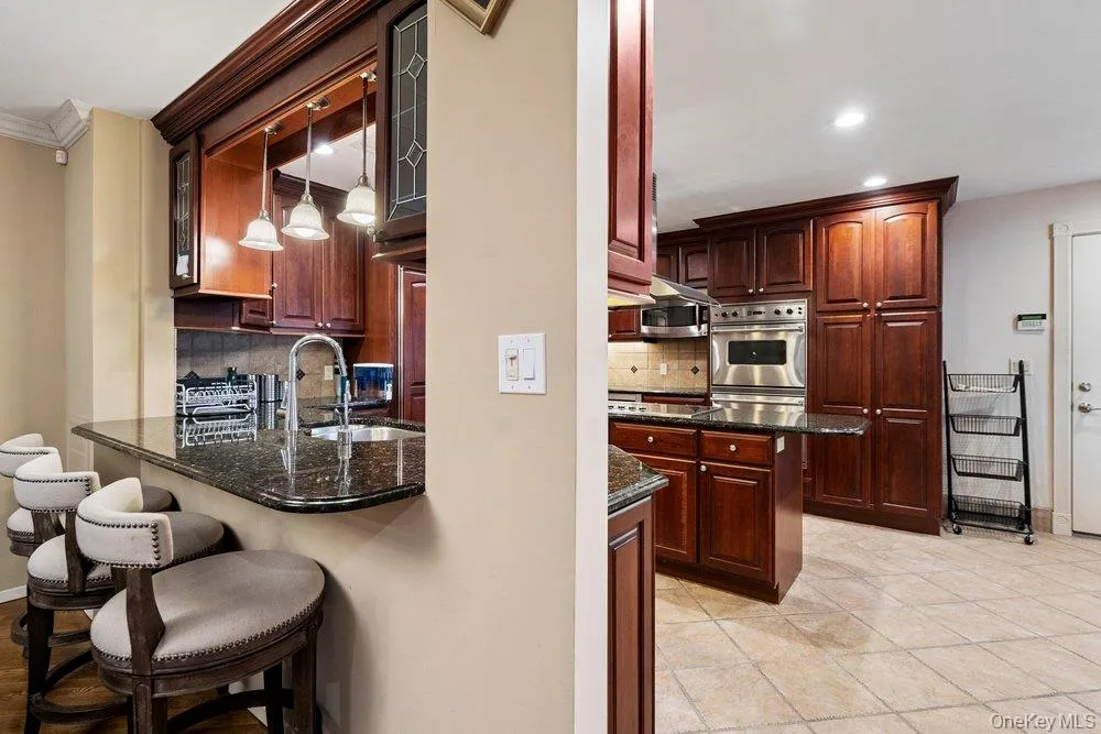 Kitchen featuring dark wood cabinetry, stainless steel appliances, a granite countertop, and a breakfast bar with pendant lighting Kitchen featuring dark wood cabinetry, stainless steel appliances, a granite countertop, and a breakfast bar with pendant lighting