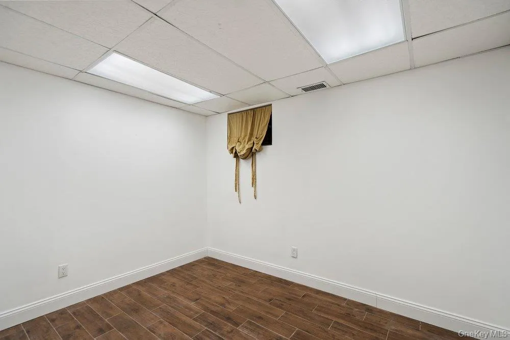 Room featuring wood-finish plank flooring, white baseboards, and a drop ceiling with recessed lighting panels Room featuring wood-finish plank flooring, white baseboards, and a drop ceiling with recessed lighting panels