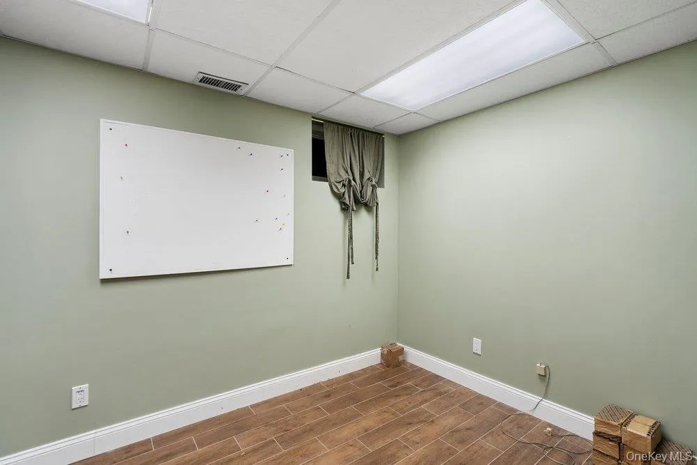Neutral wall color with crisp white trim, wood-finish flooring, and drop ceiling with integrated fluorescent lighting Neutral wall color with crisp white trim, wood-finish flooring, and drop ceiling with integrated fluorescent lighting