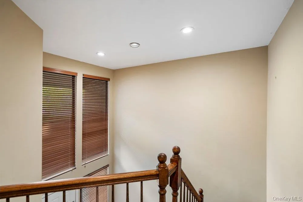Staircase featuring a rich wood-finish handrail and balusters, two tall windows with horizontal blinds, and recessed ceiling lighting Staircase featuring a rich wood-finish handrail and balusters, two tall windows with horizontal blinds, and recessed ceiling lighting