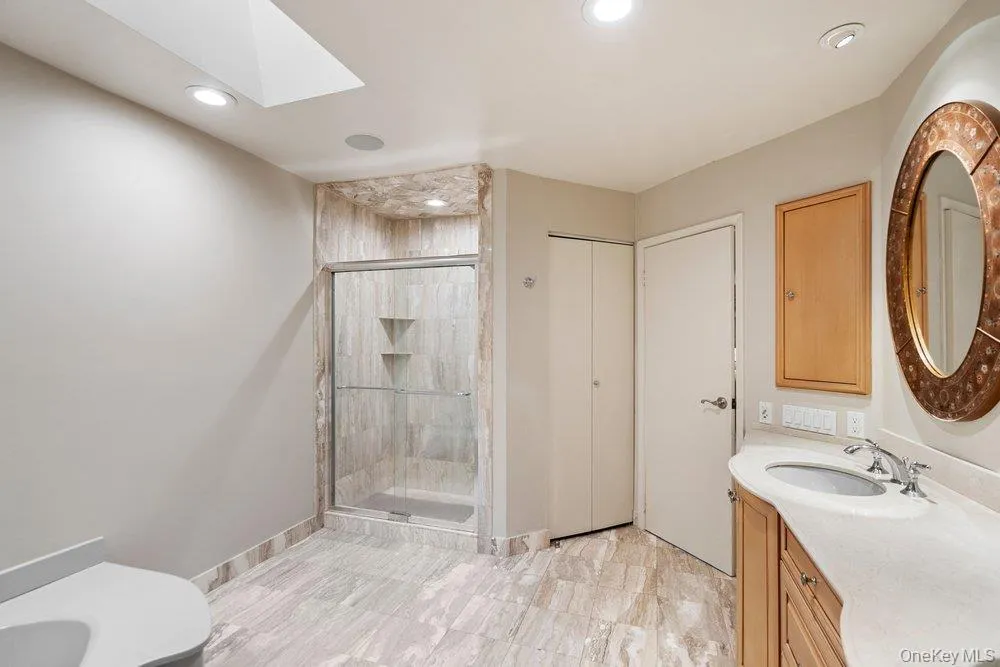 Bathroom featuring a glass-enclosed shower with integrated shelving, a skylight, recessed lighting, and stone-finish flooring Bathroom featuring a glass-enclosed shower with integrated shelving, a skylight, recessed lighting, and stone-finish flooring