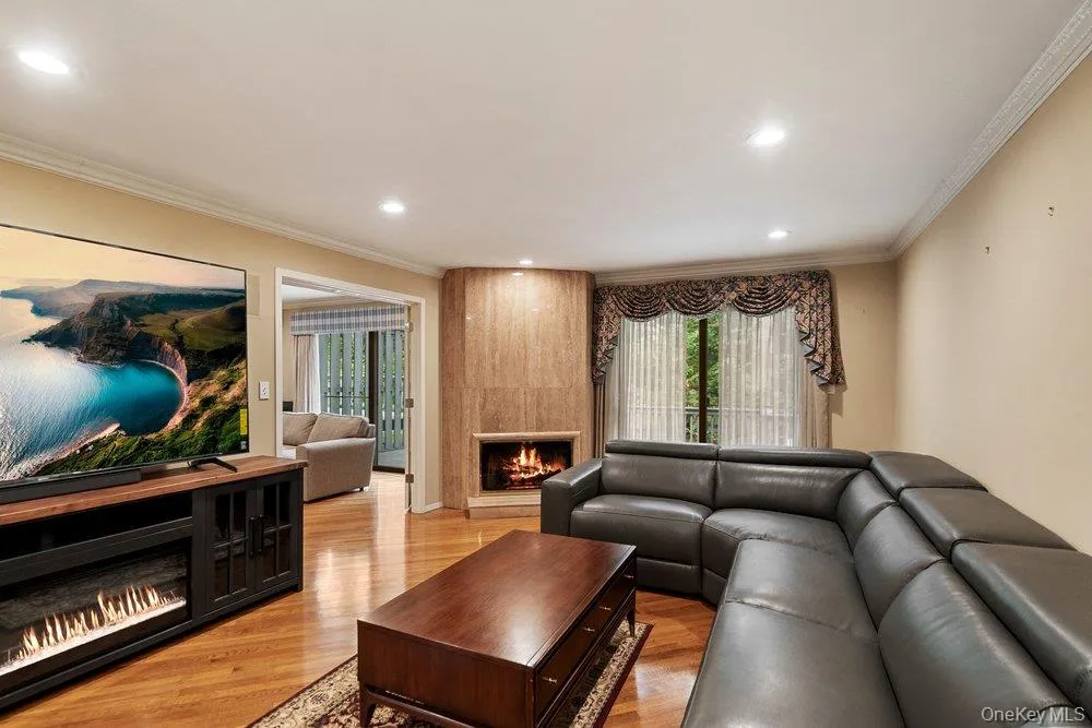 Living area featuring a corner fireplace with a stone surround, hardwood flooring, recessed lighting, and crown molding Living area featuring a corner fireplace with a stone surround, hardwood flooring, recessed lighting, and crown molding