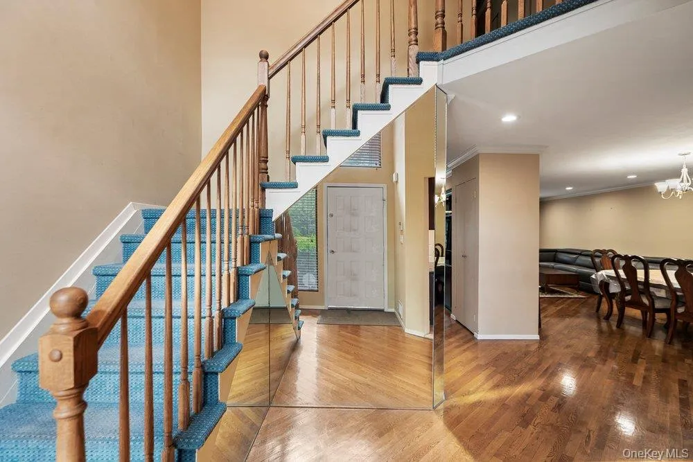 Two-story entryway featuring a wood staircase with blue carpeted treads, mirrored wall accents, and wood-finish flooring Two-story entryway featuring a wood staircase with blue carpeted treads, mirrored wall accents, and wood-finish flooring