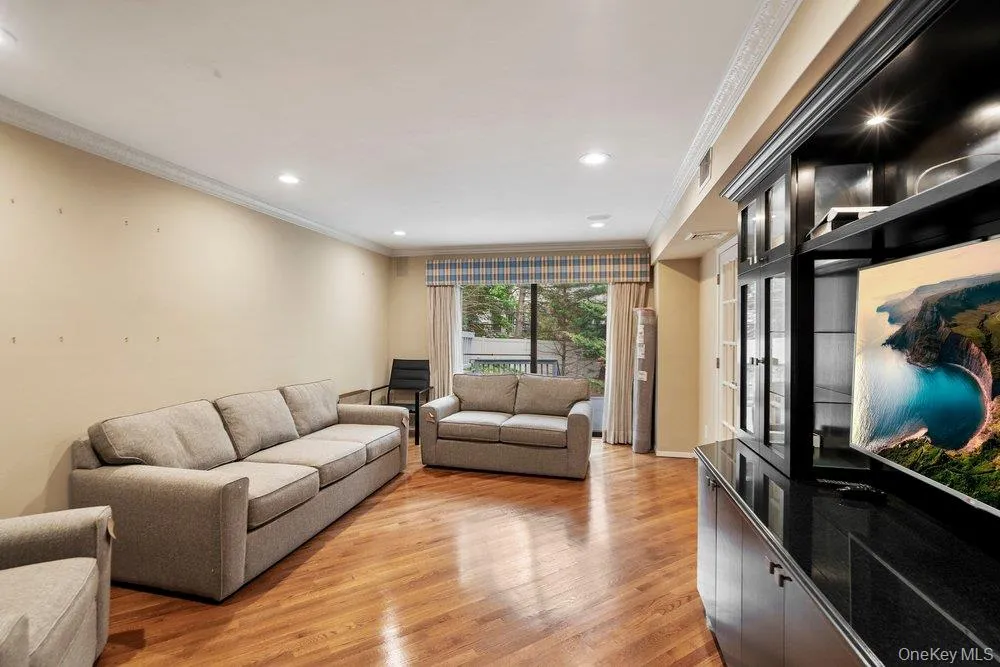 Spacious living area featuring warm wood-finish flooring, recessed lighting, and crown molding Spacious living area featuring warm wood-finish flooring, recessed lighting, and crown molding