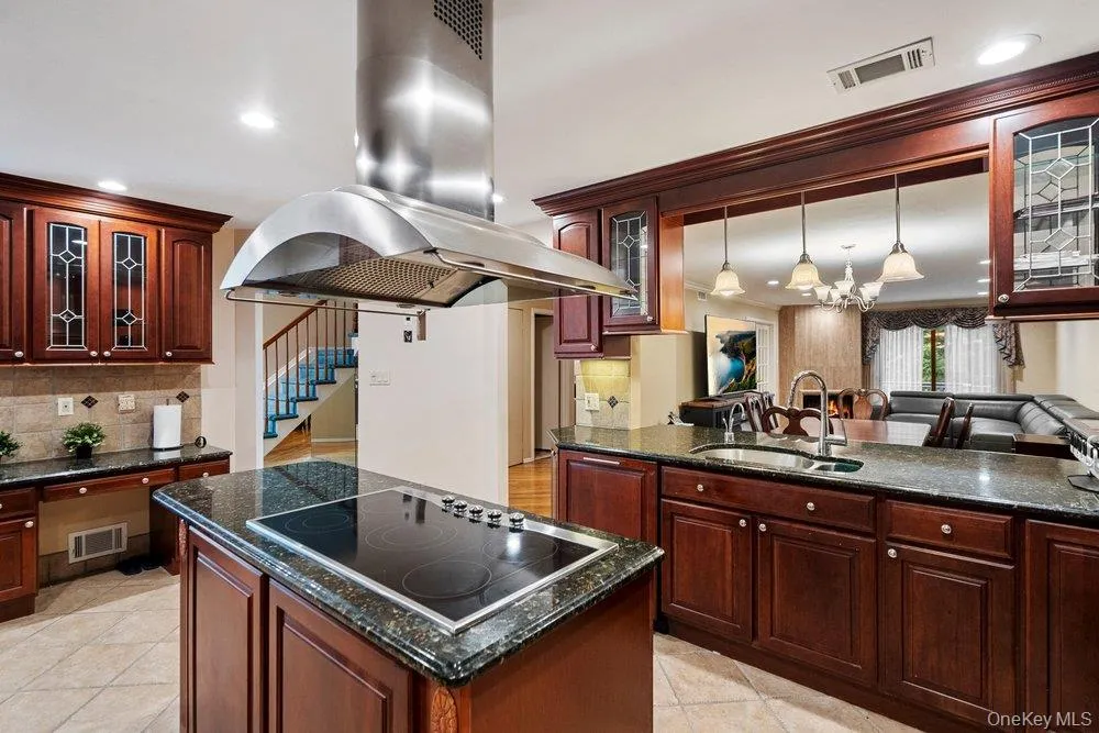 Gourmet kitchen featuring a central island with an electric cooktop, stainless steel range hood, stone countertops, and extensive wood cabinetry Gourmet kitchen featuring a central island with an electric cooktop, stainless steel range hood, stone countertops, and extensive wood cabinetry