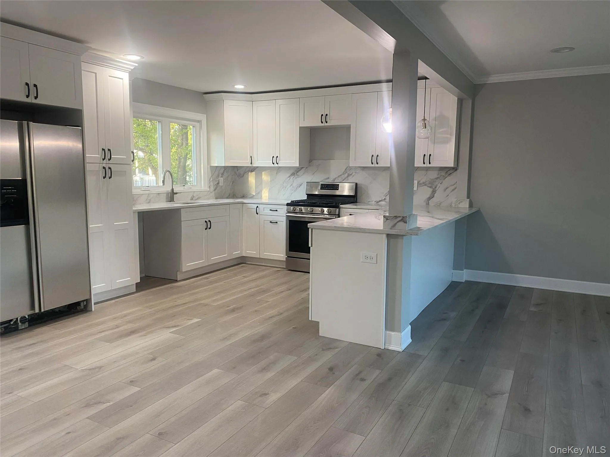 Contemporary kitchen featuring white shaker cabinetry, stainless steel appliances, quartz countertops and backsplash, and a breakfast bar Contemporary kitchen featuring white shaker cabinetry, stainless steel appliances, quartz countertops and backsplash, and a breakfast bar