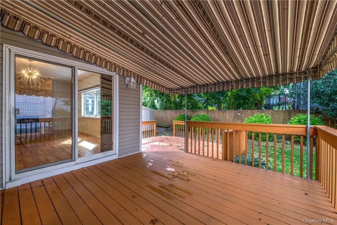 Expansive wood-finish deck featuring a striped retractable awning, wood railing, and direct access to interior via sliding glass doors Expansive wood-finish deck featuring a striped retractable awning, wood railing, and direct access to interior via sliding glass doors