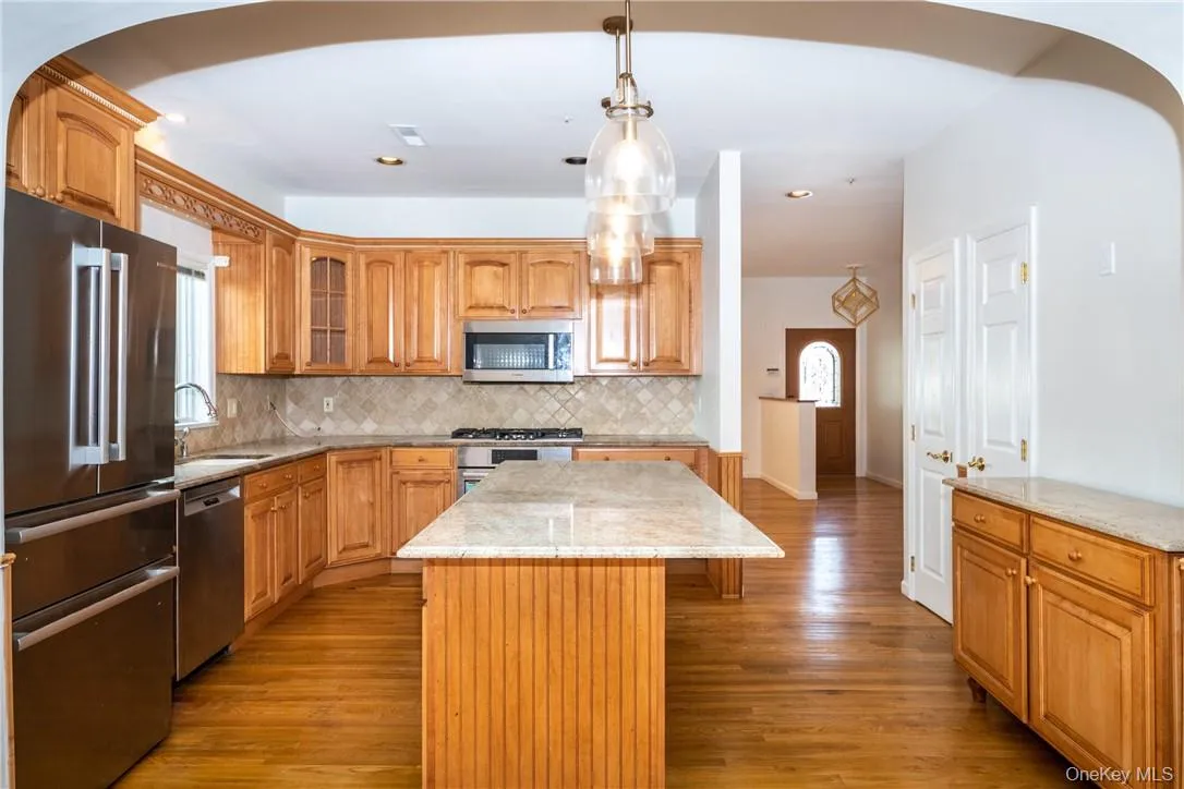 Kitchen featuring wood-finish cabinetry, stainless steel appliances, and an island with a light-toned countertop Kitchen featuring wood-finish cabinetry, stainless steel appliances, and an island with a light-toned countertop