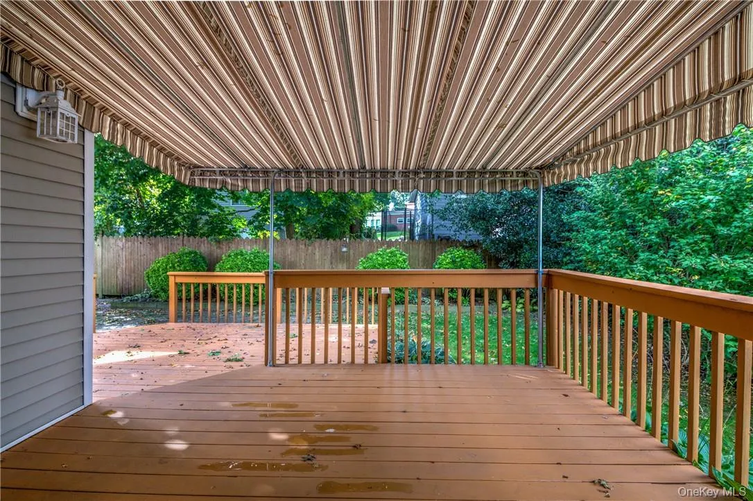 Spacious wooden deck featuring a striped retractable awning, wood railing, and a side-mounted lantern light fixture Spacious wooden deck featuring a striped retractable awning, wood railing, and a side-mounted lantern light fixture