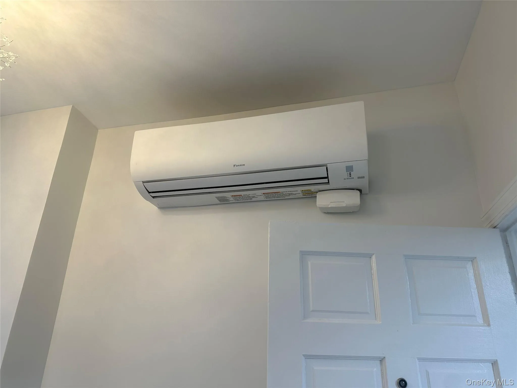 Wall-mounted mini-split system positioned above a paneled interior door, featuring a white finish Wall-mounted mini-split system positioned above a paneled interior door, featuring a white finish