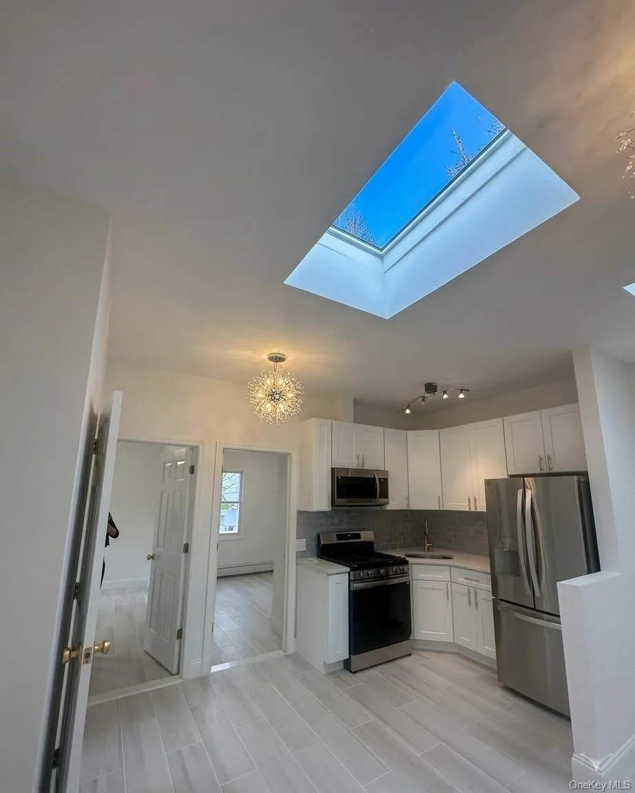 Kitchen space featuring a prominent skylight, wood-finish flooring, white cabinetry, stainless steel appliances, and a tiled backsplash Kitchen space featuring a prominent skylight, wood-finish flooring, white cabinetry, stainless steel appliances, and a tiled backsplash