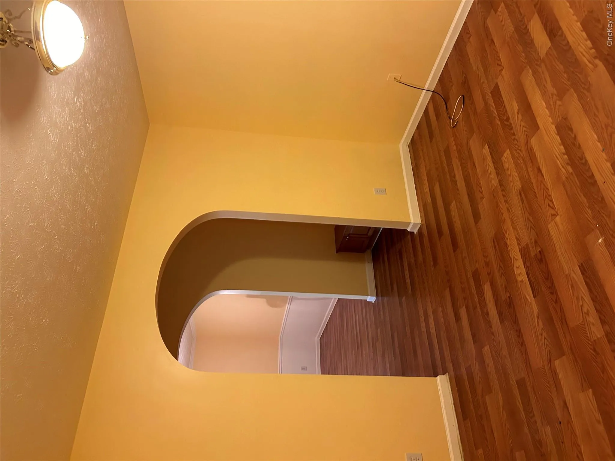 Wood-finish flooring throughout, complemented by a recessed arched doorway, white baseboards, and a semi-flush mount ceiling light fixture Wood-finish flooring throughout, complemented by a recessed arched doorway, white baseboards, and a semi-flush mount ceiling light fixture