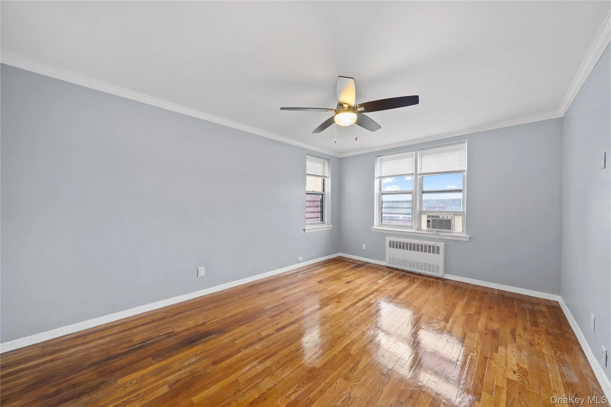 Spacious room featuring wood-finish flooring, light blue walls, and a ceiling fan with integrated lighting Spacious room featuring wood-finish flooring, light blue walls, and a ceiling fan with integrated lighting