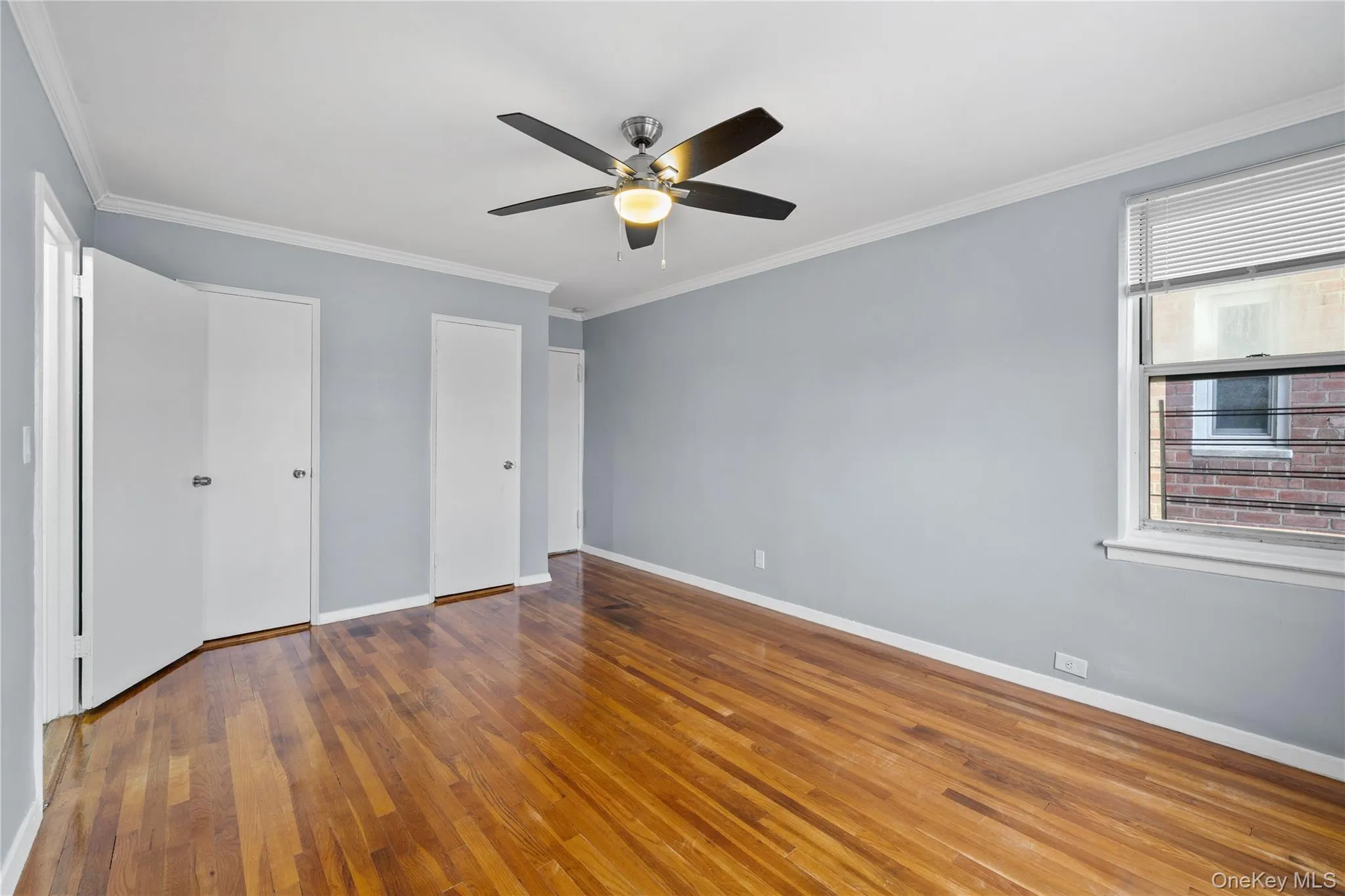 Spacious room featuring wood-finish flooring, a ceiling fan with light fixture, multiple doors, and a window with blinds Spacious room featuring wood-finish flooring, a ceiling fan with light fixture, multiple doors, and a window with blinds