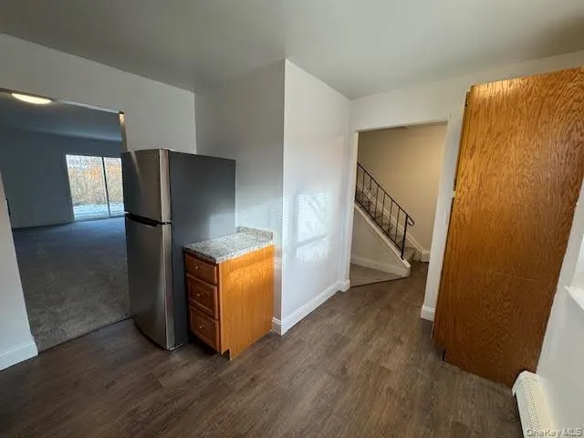 Kitchen with brown cabinetry, freestanding refrigerator, dark wood-type flooring, and light stone countertops Kitchen with brown cabinetry, freestanding refrigerator, dark wood-type flooring, and light stone countertops