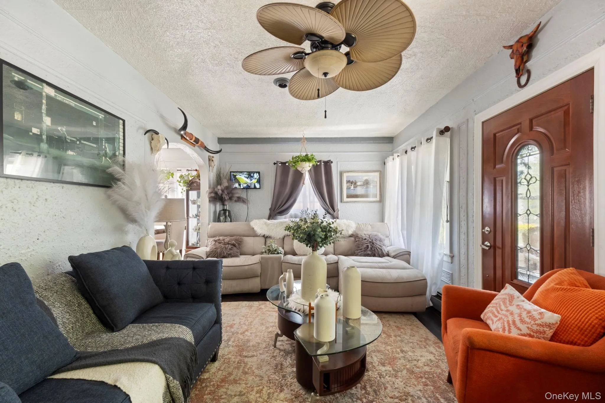 Interior living space featuring a decorative ceiling fan, wood-finish entry door with leaded glass, light-toned wall paneling, and a patterned area rug Interior living space featuring a decorative ceiling fan, wood-finish entry door with leaded glass, light-toned wall paneling, and a patterned area rug