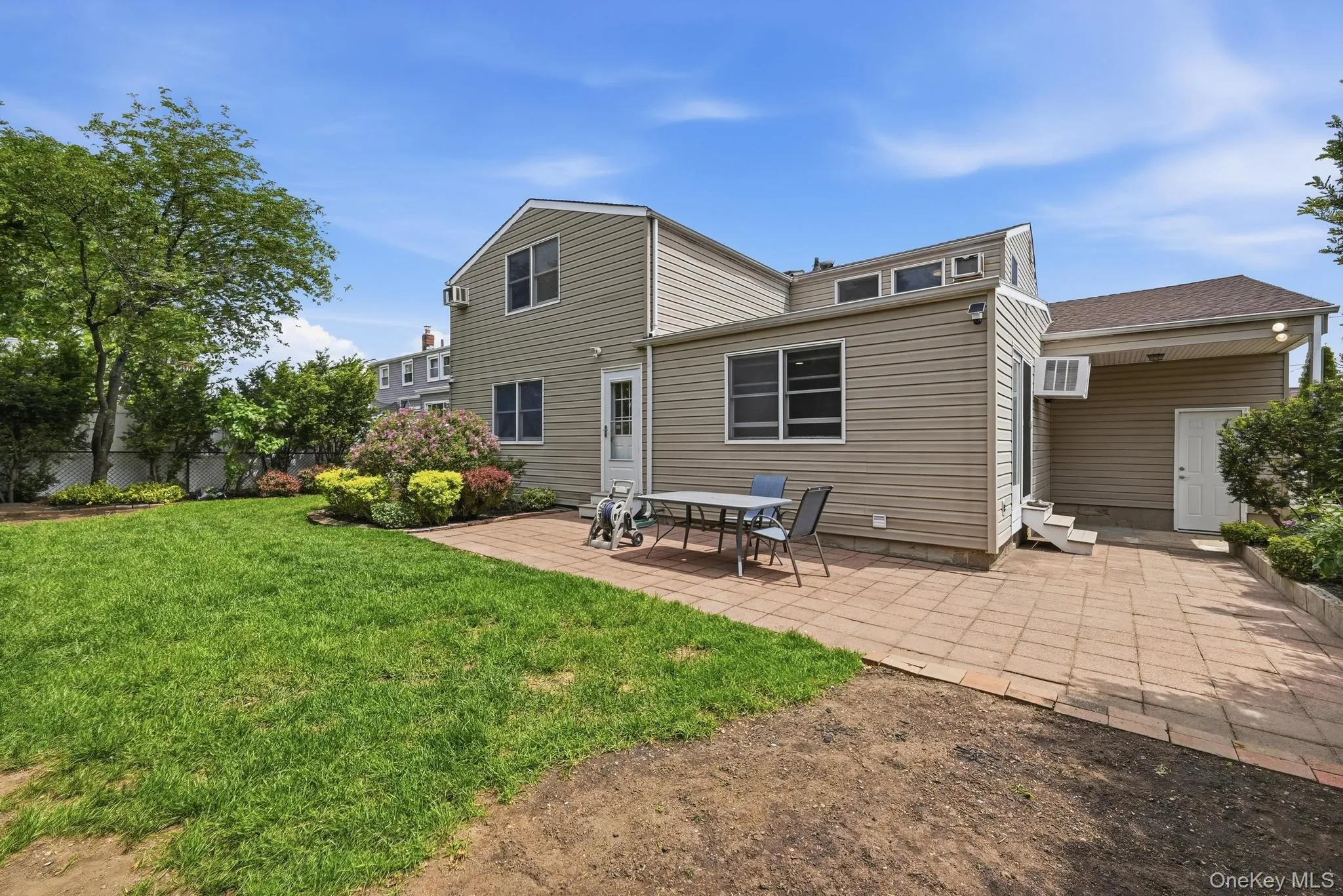 Spacious backyard featuring a large paver patio, lush green lawn, mature trees, and established shrubbery Spacious backyard featuring a large paver patio, lush green lawn, mature trees, and established shrubbery