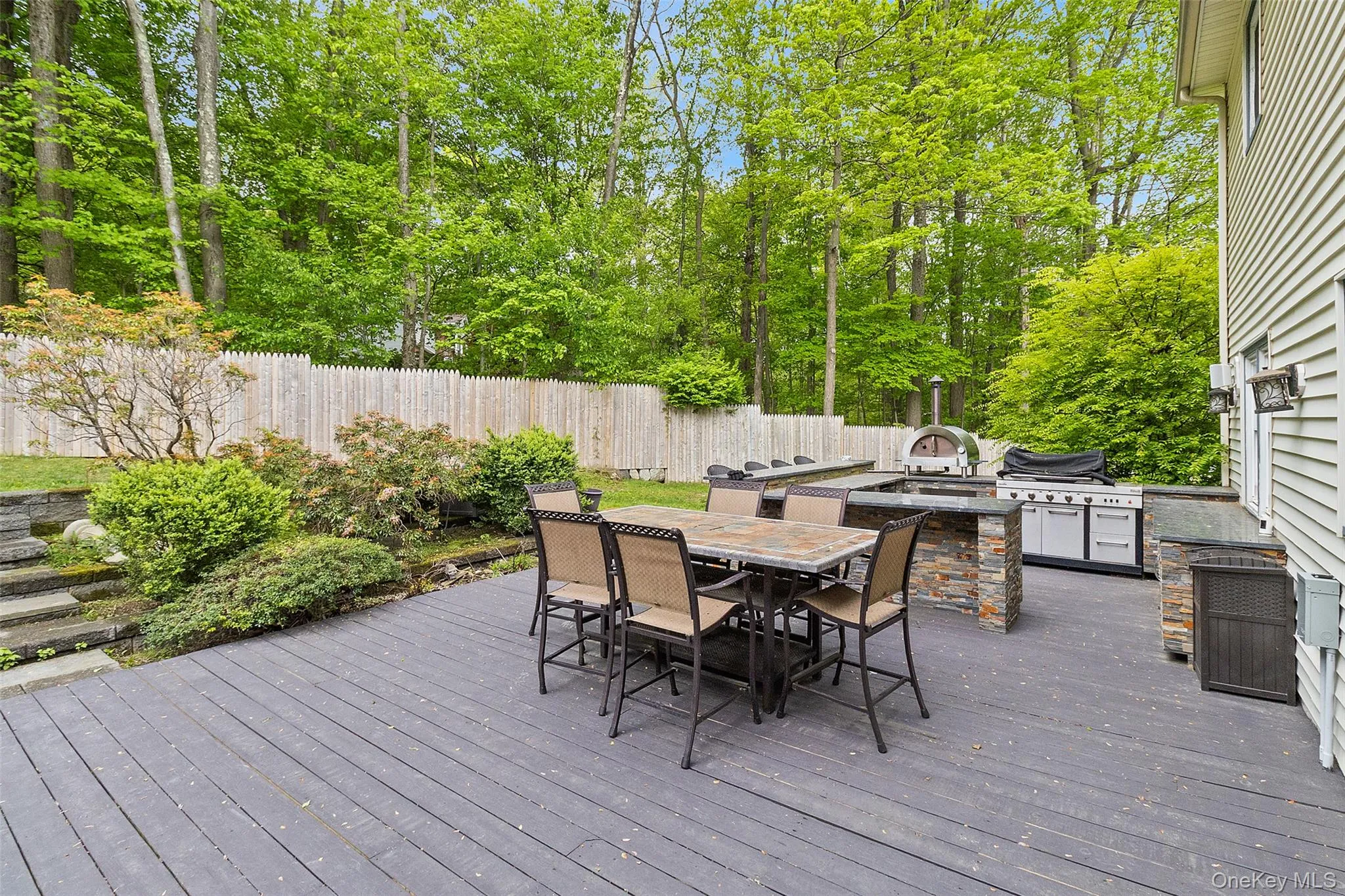 Spacious outdoor deck featuring an integrated outdoor kitchen with a built-in pizza oven, grill, and stone-clad base Spacious outdoor deck featuring an integrated outdoor kitchen with a built-in pizza oven, grill, and stone-clad base