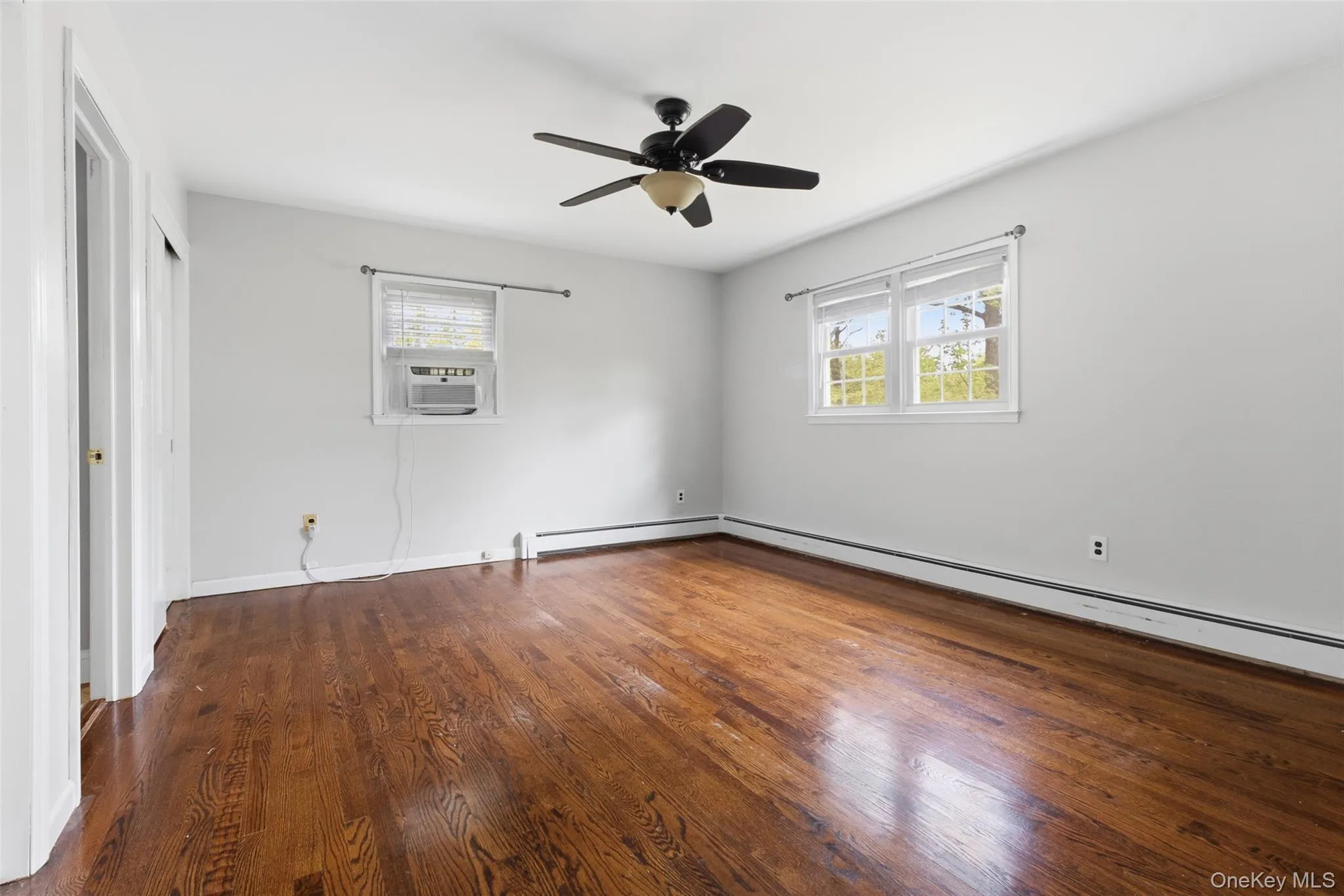 Spacious room featuring rich wood-finish flooring, light gray wall paint, and white trim Spacious room featuring rich wood-finish flooring, light gray wall paint, and white trim