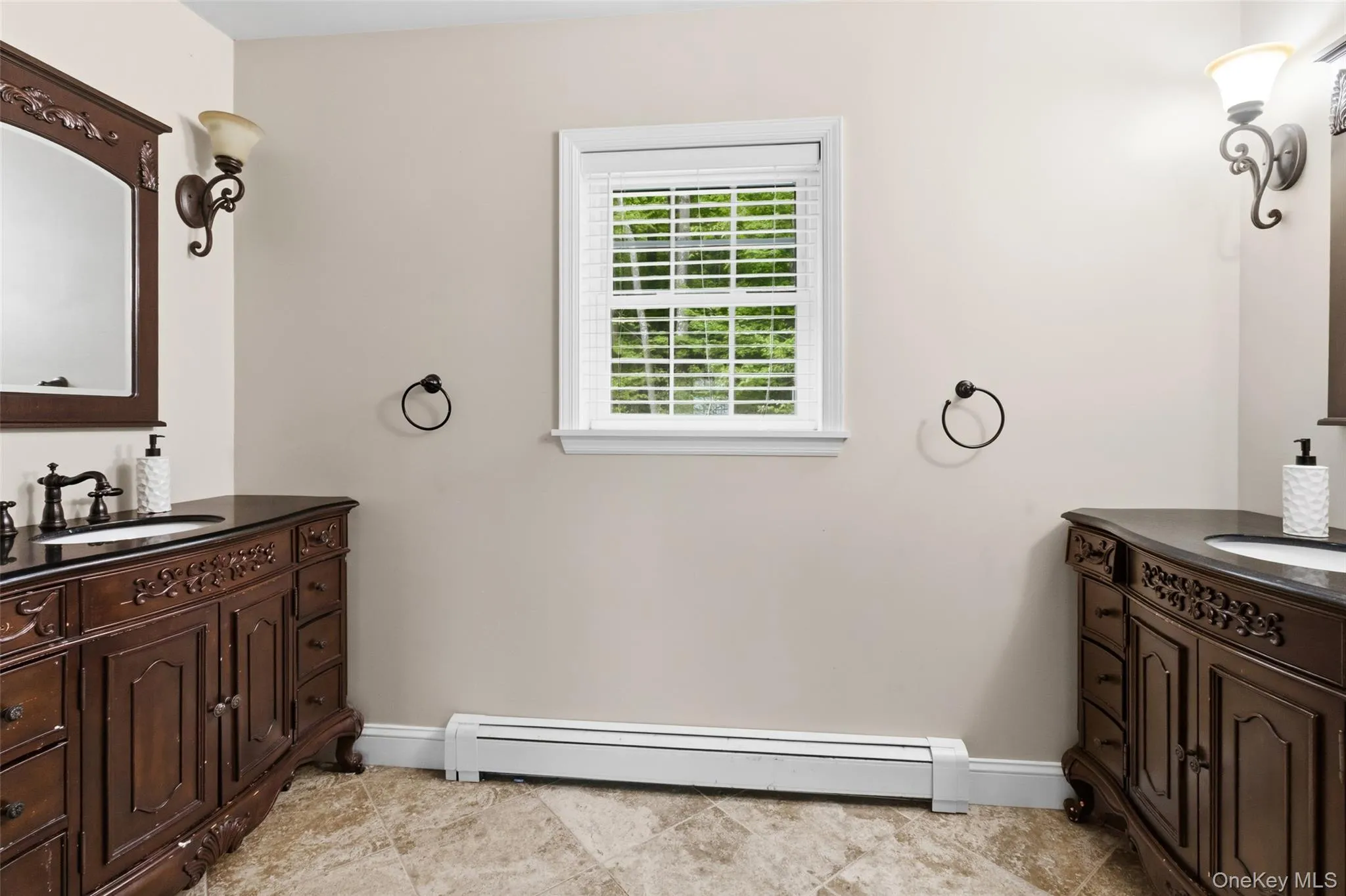 Dual dark wood vanities featuring integrated sinks and black countertops, bronze wall sconces, and a window Dual dark wood vanities featuring integrated sinks and black countertops, bronze wall sconces, and a window