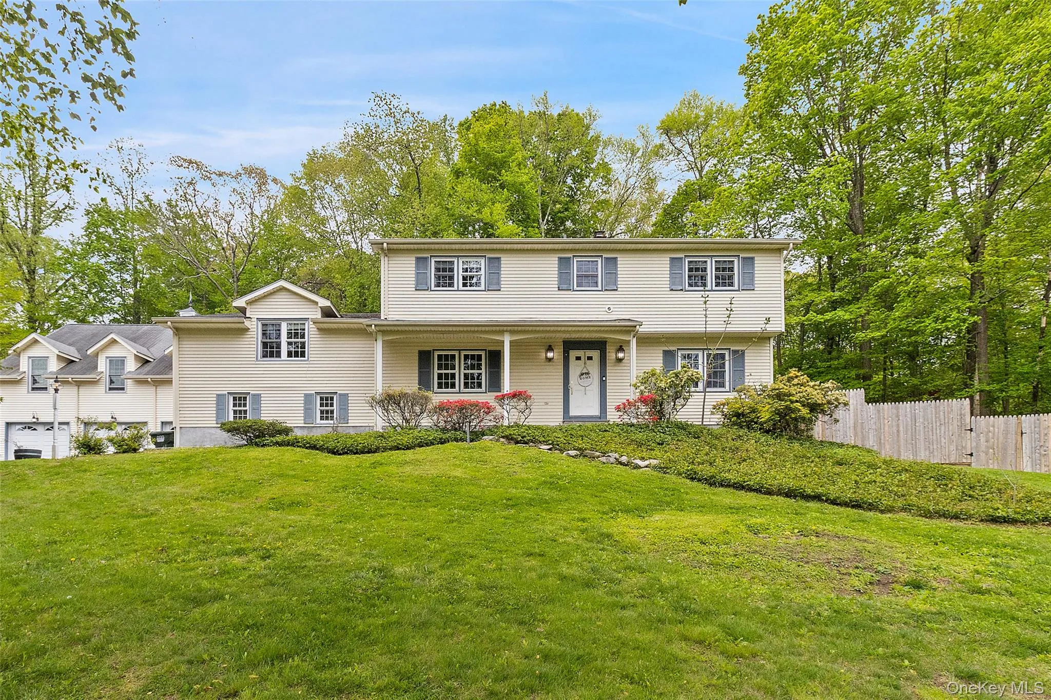 Split-level home featuring light-colored siding, blue window shutters, a covered front porch, and an attached two-car garage Split-level home featuring light-colored siding, blue window shutters, a covered front porch, and an attached two-car garage