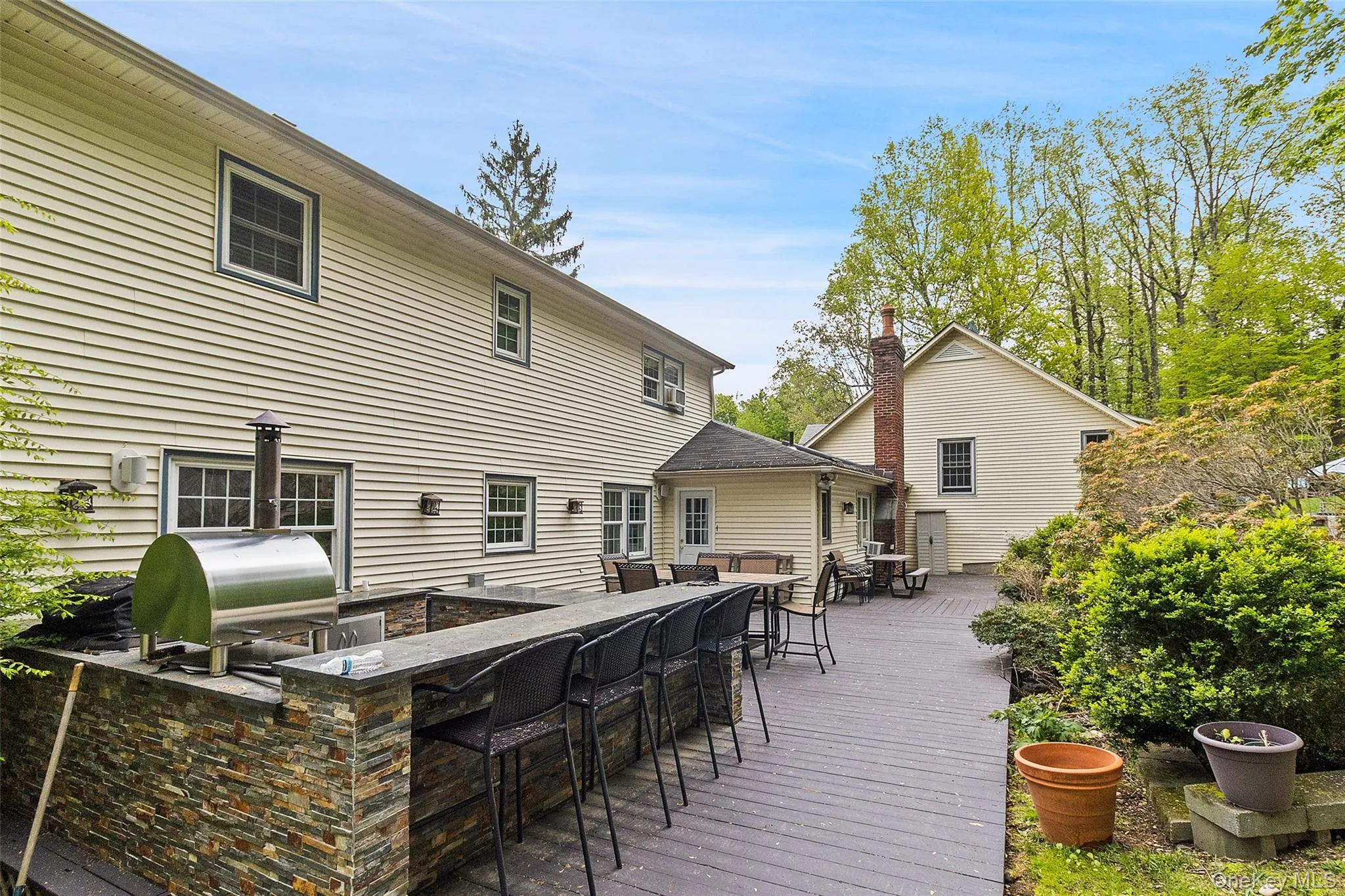 Expansive outdoor living area featuring a multi-level composite deck, built-in stone veneer outdoor kitchen with a stainless steel pizza oven, and a stone-clad bar with seating Expansive outdoor living area featuring a multi-level composite deck, built-in stone veneer outdoor kitchen with a stainless steel pizza oven, and a stone-clad bar with seating
