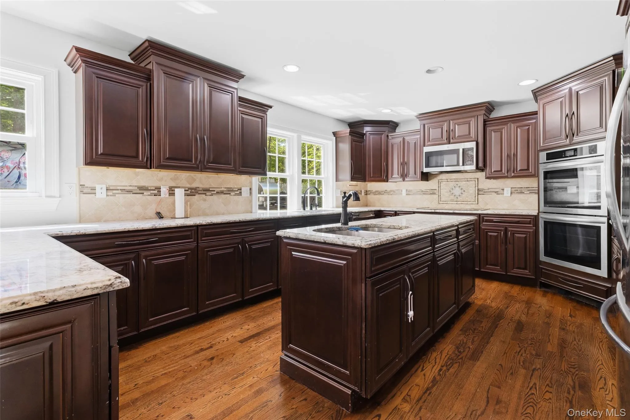 Kitchen featuring dark wood cabinetry, light-colored countertops, hardwood flooring, and stainless steel double ovens Kitchen featuring dark wood cabinetry, light-colored countertops, hardwood flooring, and stainless steel double ovens
