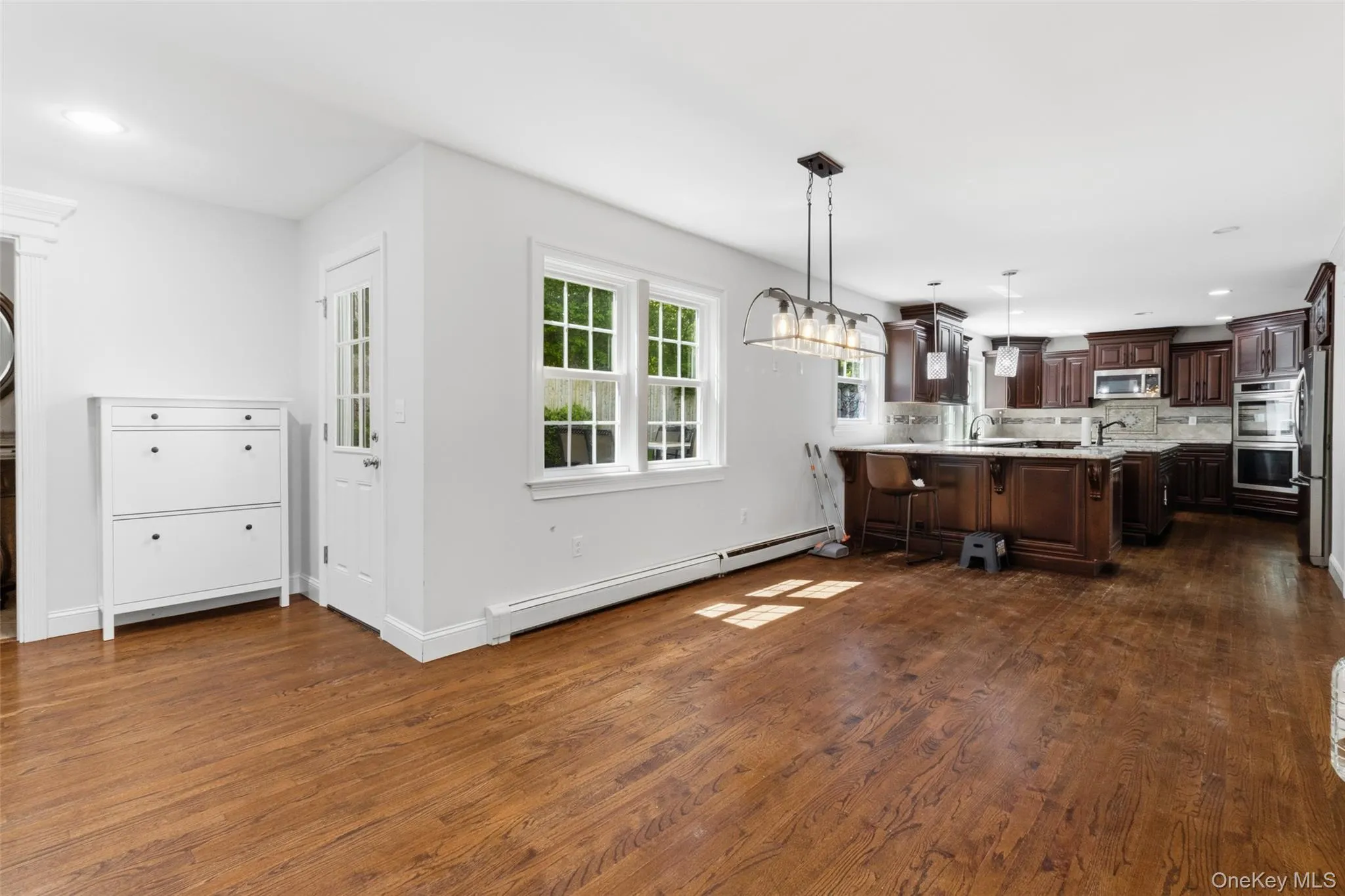 Open-concept kitchen and dining area featuring wood-finish flooring, white trim, and a window with grid detailing Open-concept kitchen and dining area featuring wood-finish flooring, white trim, and a window with grid detailing