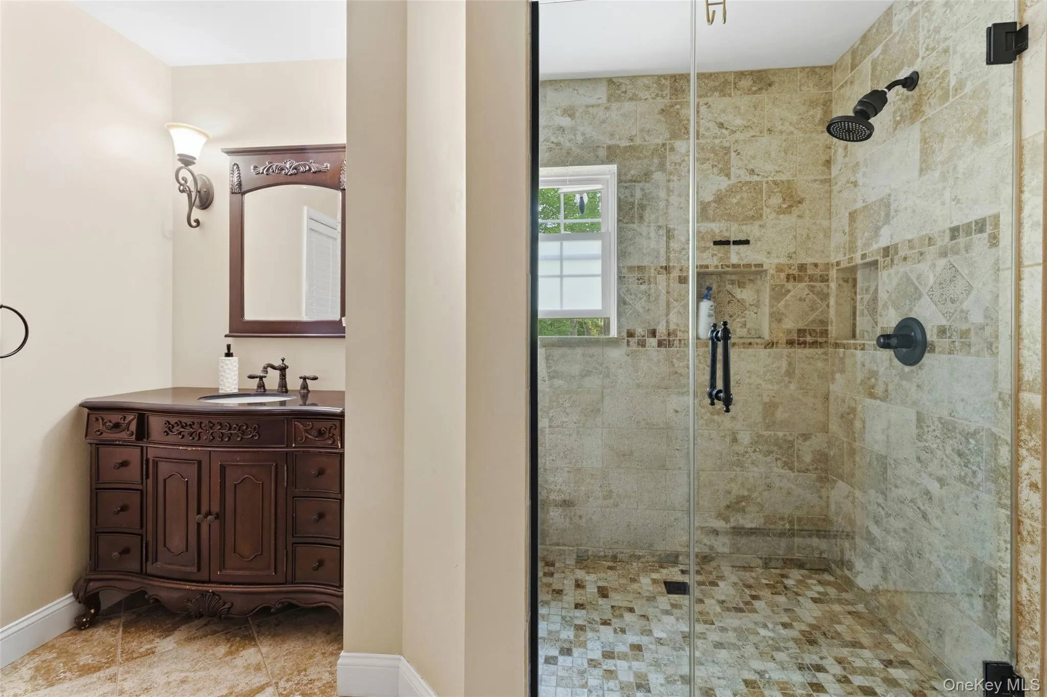 Glass-enclosed shower with mosaic tile floor and beige wall tiling featuring decorative accents Glass-enclosed shower with mosaic tile floor and beige wall tiling featuring decorative accents