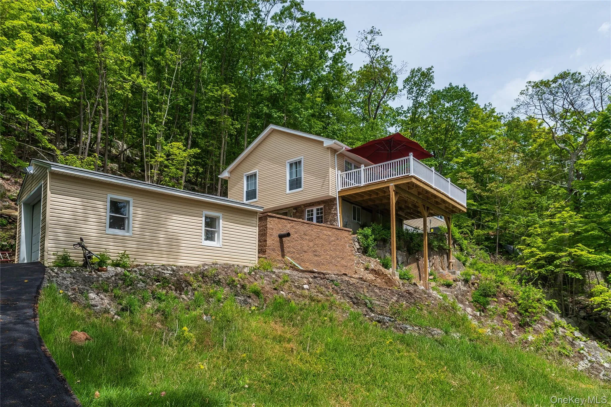 Front of property with a wooden deck, stone siding, and a garage Front of property with a wooden deck, stone siding, and a garage