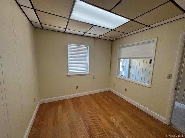 Room featuring wood-finish flooring, two windows with white blinds, a drop ceiling with recessed lighting, and light-toned walls Room featuring wood-finish flooring, two windows with white blinds, a drop ceiling with recessed lighting, and light-toned walls