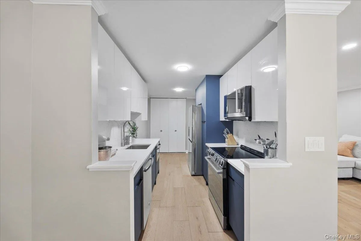 Contemporary kitchen featuring white upper cabinetry, blue lower cabinetry, stainless steel appliances, and wood-finish flooring Contemporary kitchen featuring white upper cabinetry, blue lower cabinetry, stainless steel appliances, and wood-finish flooring