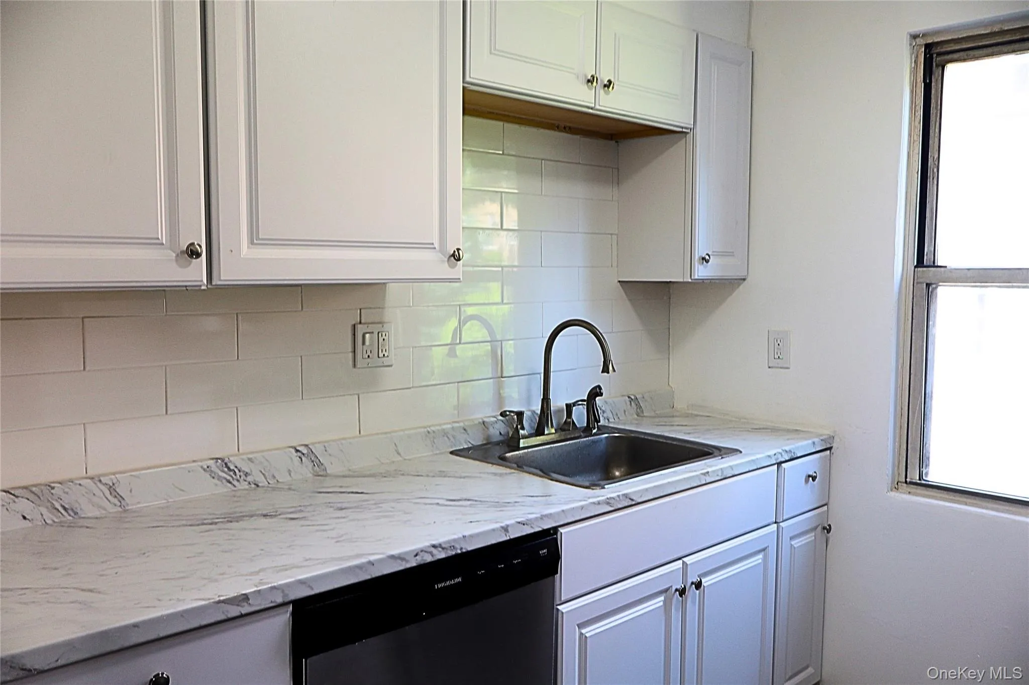 Kitchen featuring white cabinetry, subway tile backsplash, a stainless steel sink with a dark-finished faucet, and new countertops Kitchen featuring white cabinetry, subway tile backsplash, a stainless steel sink with a dark-finished faucet, and new countertops