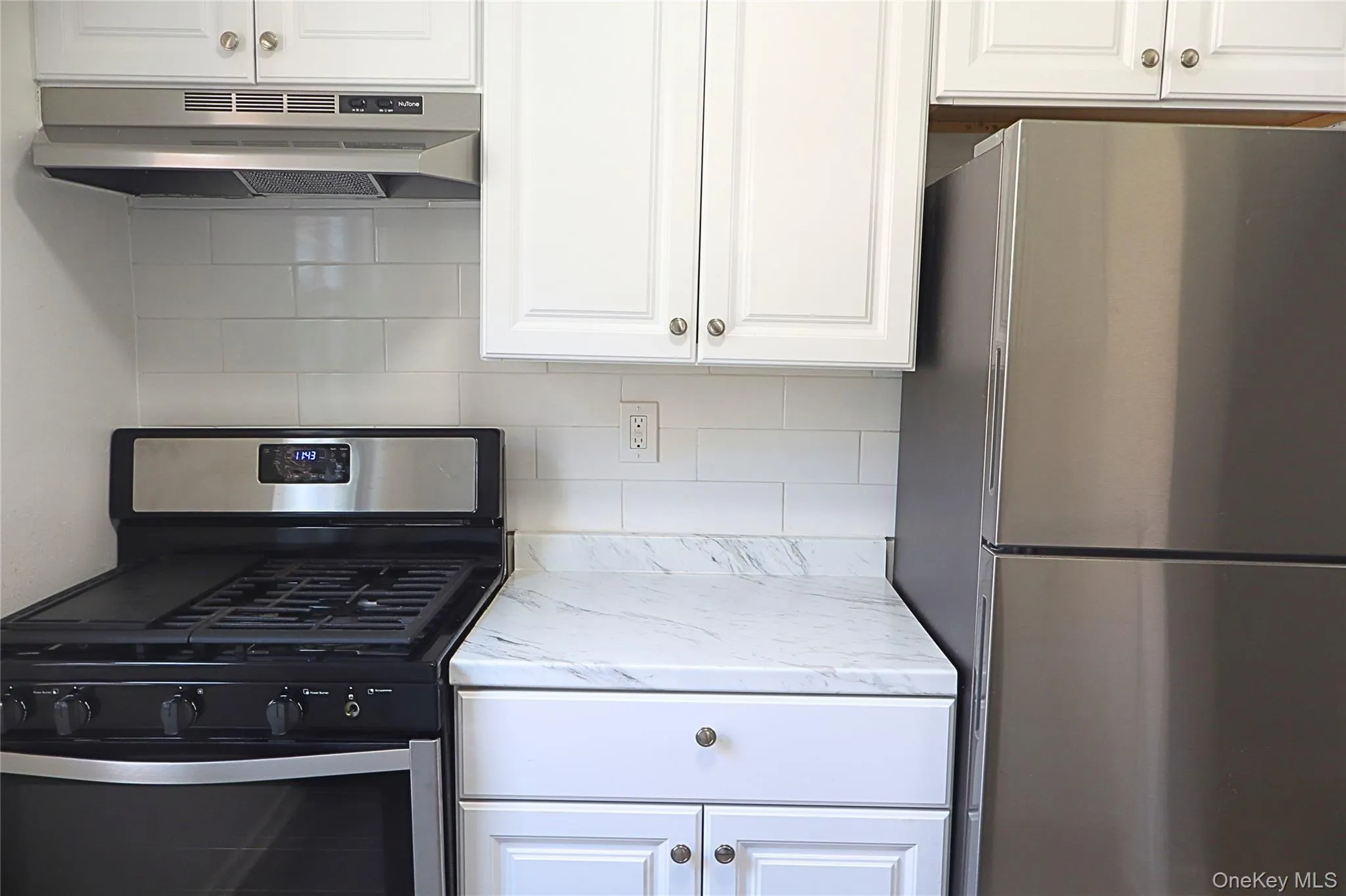Kitchen area featuring white cabinetry, a white subway tile backsplash, and a white countertop with gray veining Kitchen area featuring white cabinetry, a white subway tile backsplash, and a white countertop with gray veining