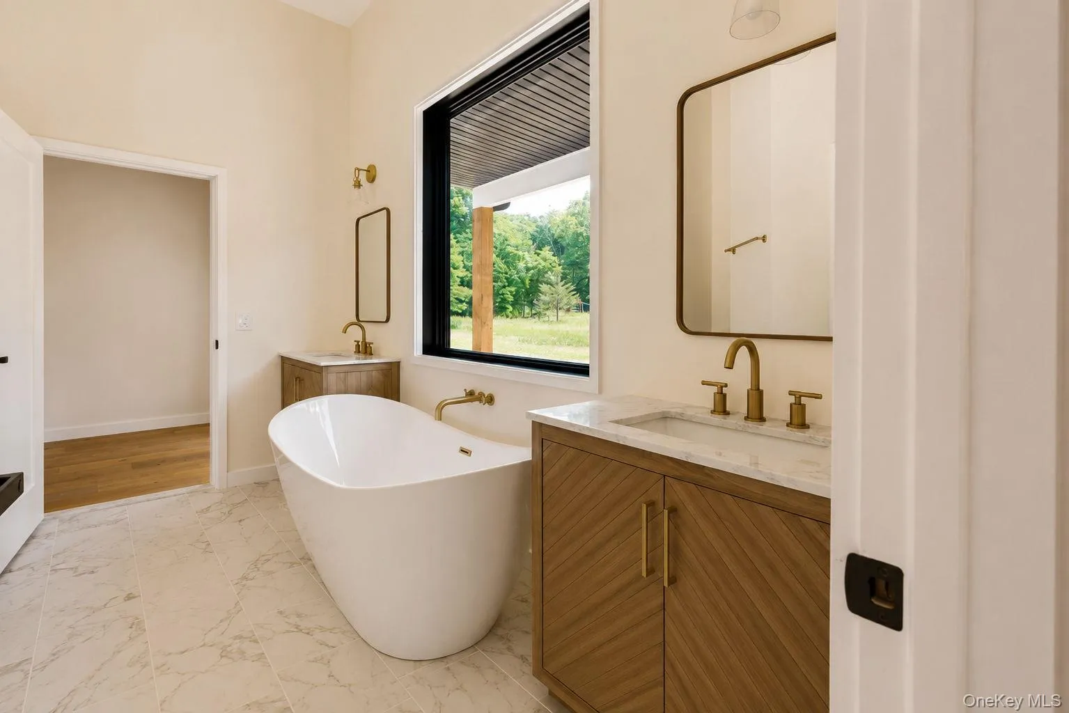 Bathroom featuring a freestanding soaking tub, dual wood-finish vanities with rectangular sinks and light-colored countertops, and gold-finish fixtures Bathroom featuring a freestanding soaking tub, dual wood-finish vanities with rectangular sinks and light-colored countertops, and gold-finish fixtures