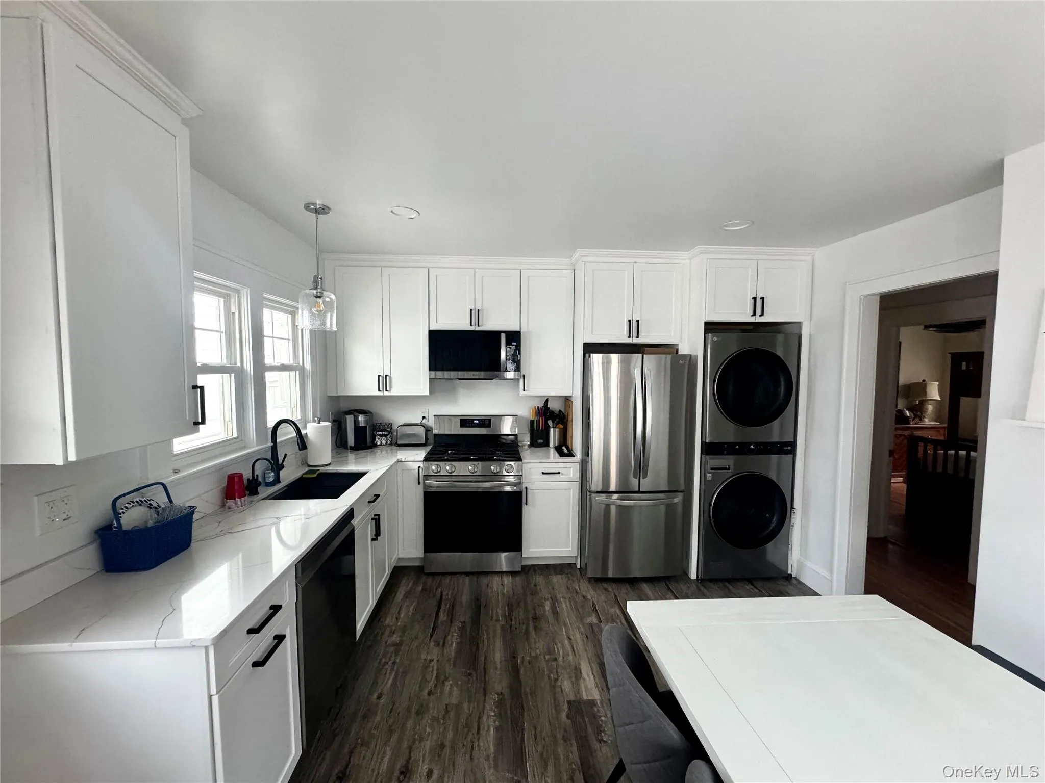 Kitchen featuring estacked washer and dryer, appliances with stainless steel finishes, dark wood-type flooring, light stone counters, and white cabinets Kitchen featuring estacked washer and dryer, appliances with stainless steel finishes, dark wood-type flooring, light stone counters, and white cabinets