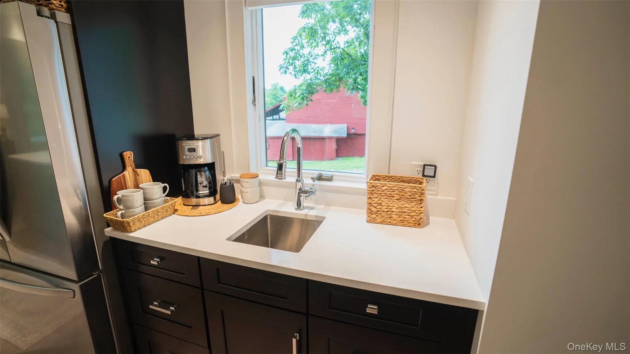 Kitchen featuring plenty of natural light, freestanding refrigerator, light countertops, and dark cabinetry Kitchen featuring plenty of natural light, freestanding refrigerator, light countertops, and dark cabinetry